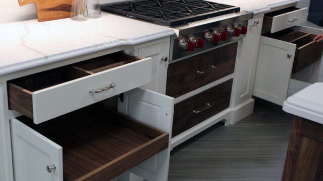 Modern kitchen with open white and wood drawers beside a stainless steel stove on a gray tiled floor.