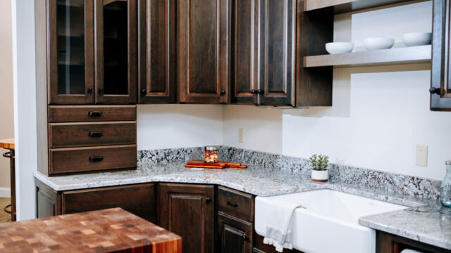 Modern kitchen with dark wood cabinets, granite countertops, a farmhouse sink, and decorative white bowls on shelves.