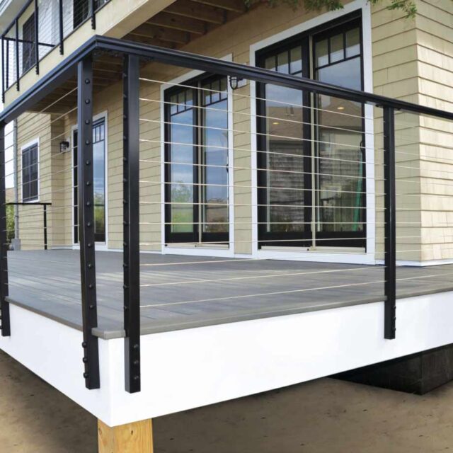 modern deck with black metal railing and wood flooring attached to a yellow house with large windows and sliding doors