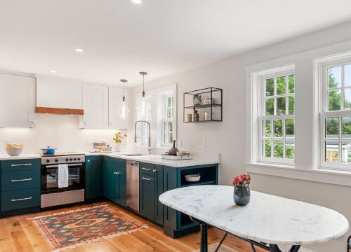 Modern kitchen with dark cabinets, white countertops, wooden floor, and natural light from large windows.