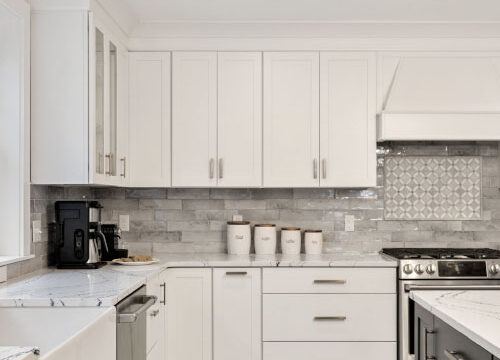 modern kitchen with white cabinets, gray tile backsplash, marble countertops, stainless steel appliances, and farmhouse sink