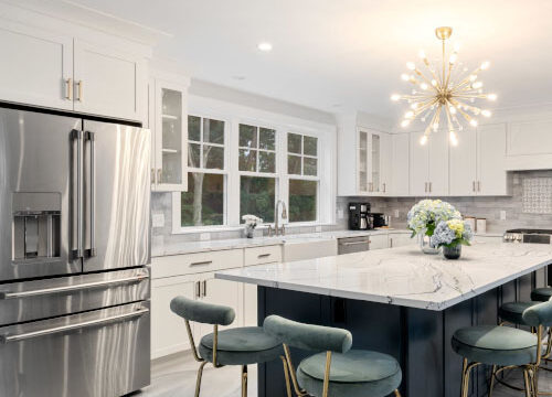 Modern kitchen with stainless steel appliances, marble island, green stools, and a starburst chandelier.
