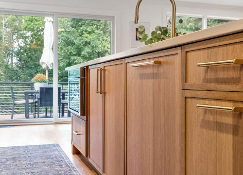 Modern kitchen with wooden cabinets, sleek handles, and a view of a lush garden through large sliding glass doors