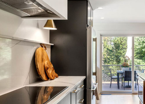 Modern kitchen with black cabinets, marble countertops, and a view of a balcony with outdoor seating through glass doors.