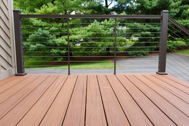 Wooden deck with modern metal railing overlooking trees and a road.