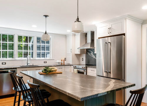 Modern kitchen with large island, stainless steel appliances, white cabinets, and wooden floors.