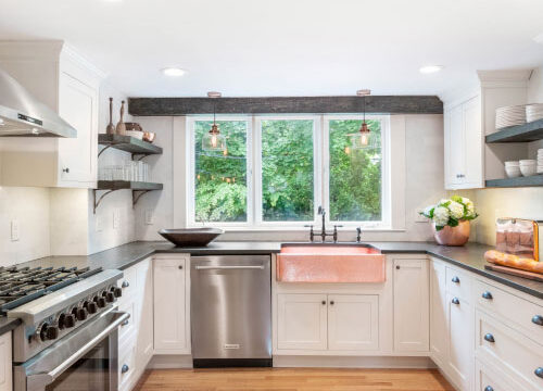Modern kitchen with copper sink, stainless steel appliances, white cabinets, and large window overlooking green trees