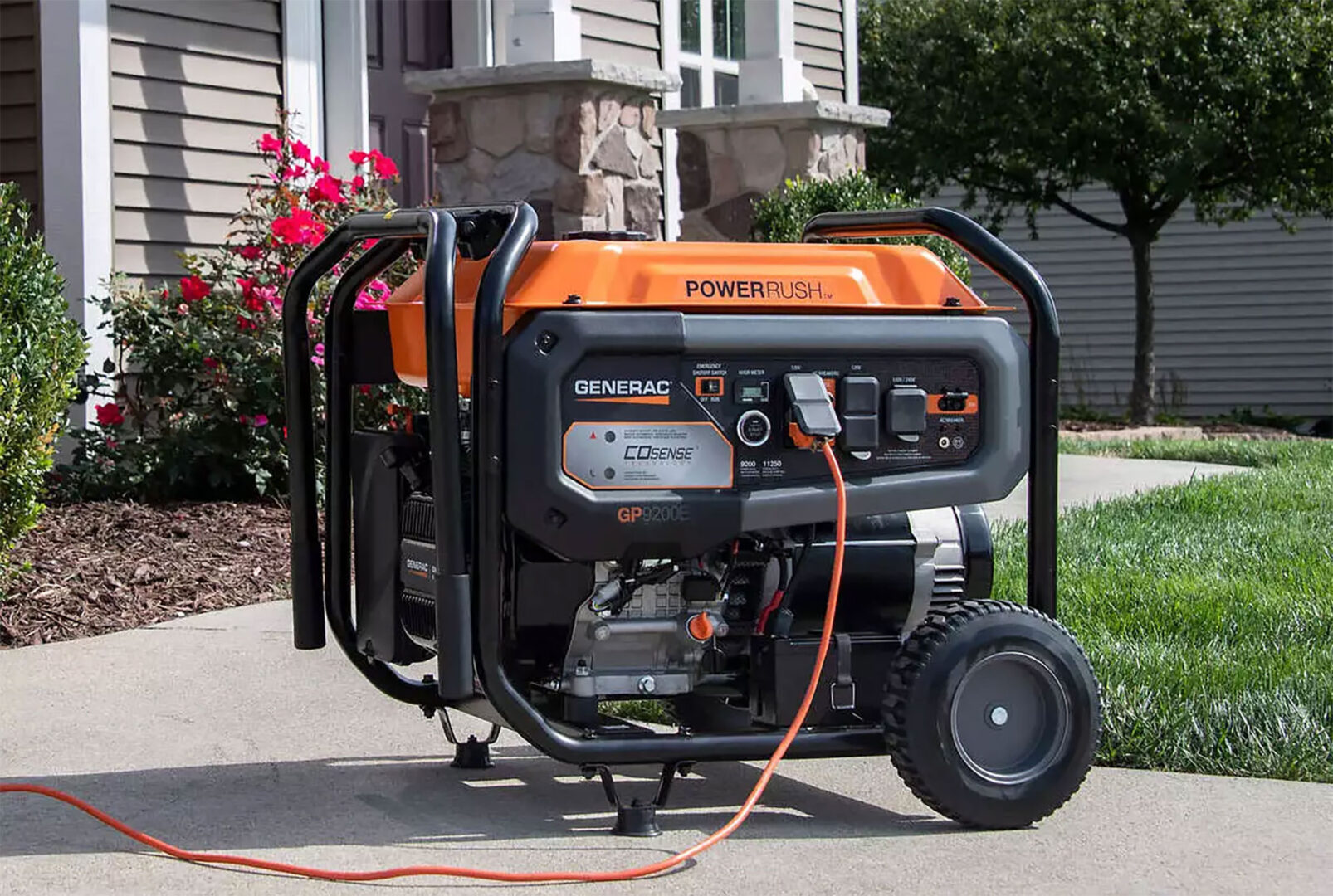 Portable orange and black generator on wheels connected with a power cord outside a house.