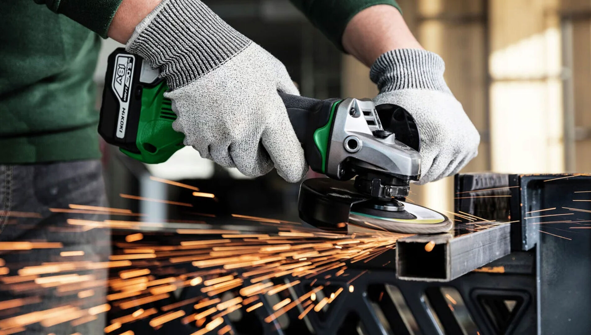 Worker using an angle grinder to cut metal, with sparks flying in a workshop setting.