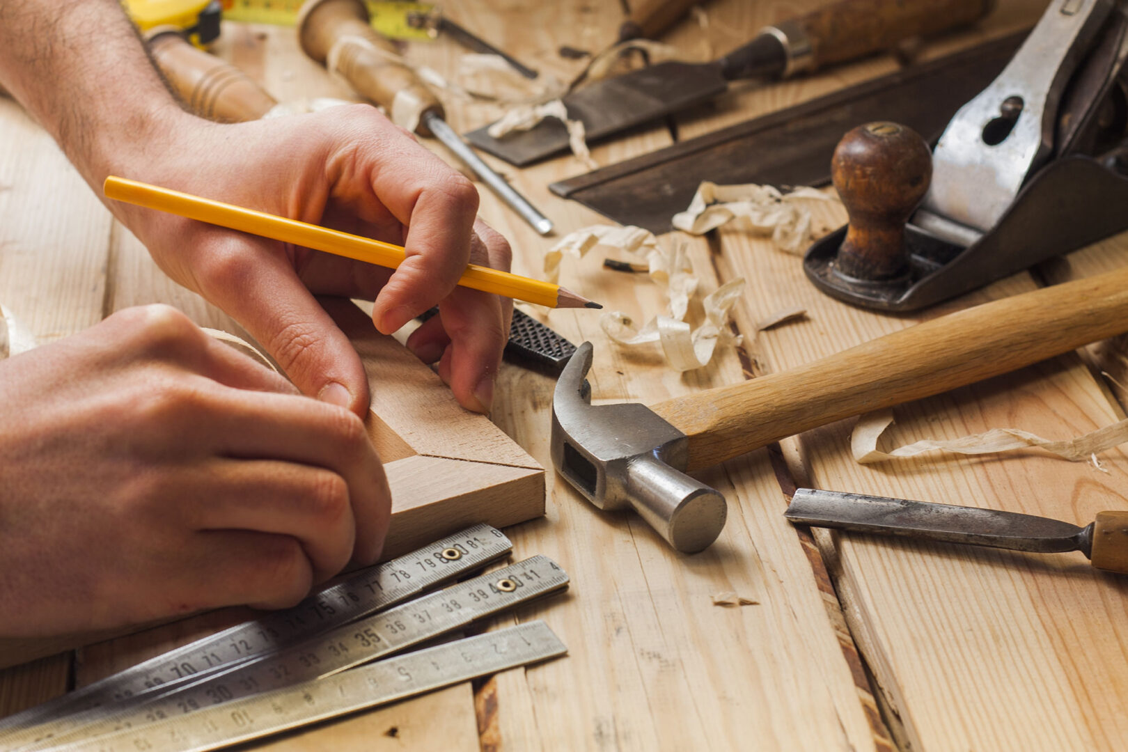 Carpenter marking wood with pencil on workbench, surrounded by tools like hammer, chisel, and shavings.