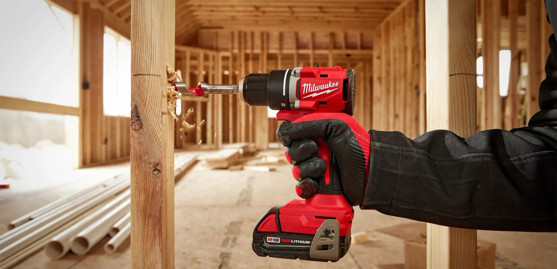 Red power drill being used to drive a screw into wooden beam in a partially constructed building.