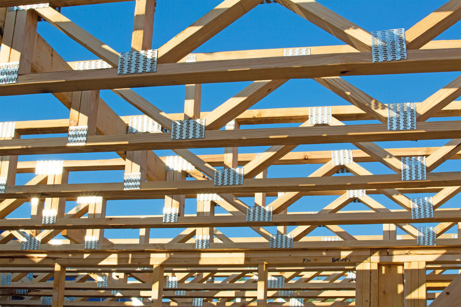 Wooden roof trusses under construction against a clear blue sky.