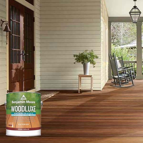 Freshly stained wooden porch with rocking chairs, a small table with a plant, and a can of wood stain in the foreground.