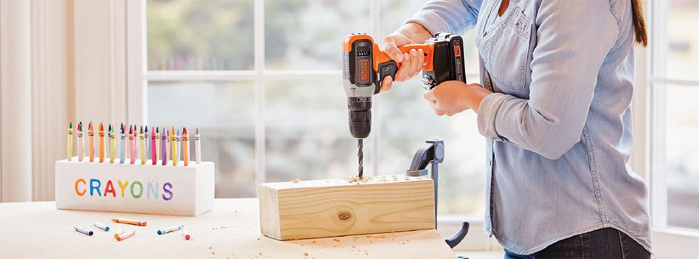 Person using a cordless drill to create a hole in a wooden block on a workbench.