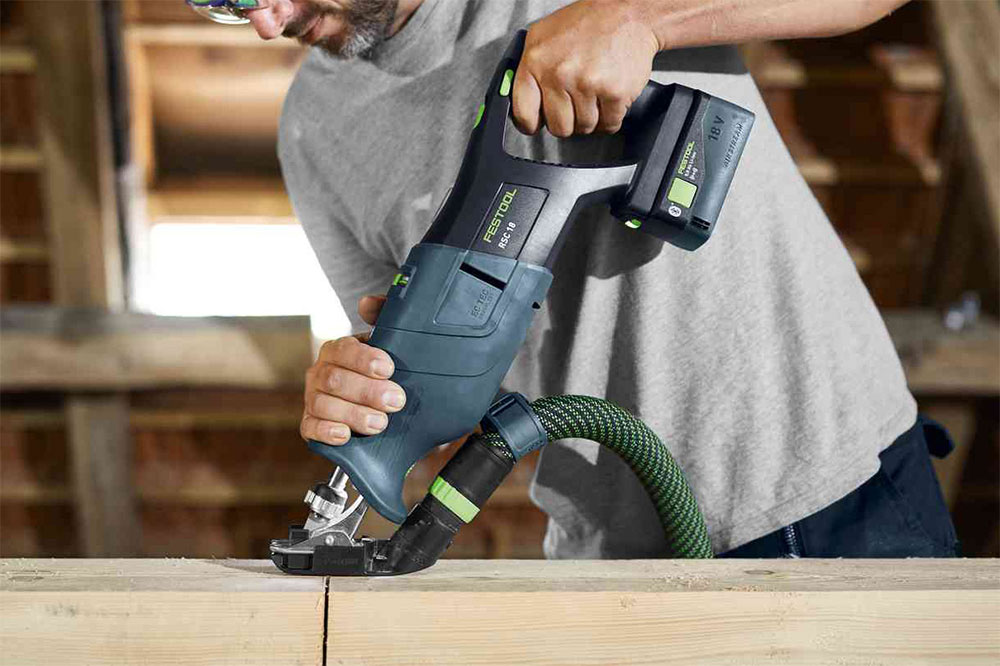 Person using a handheld power saw to cut wood in a workshop.